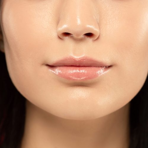 Beautiful young woman's full lips close-up shot. Female model with well-kept skin and hair. Perfect skincare, human emotions, facial expression, beauty and cosmetics concept. Looks calm.